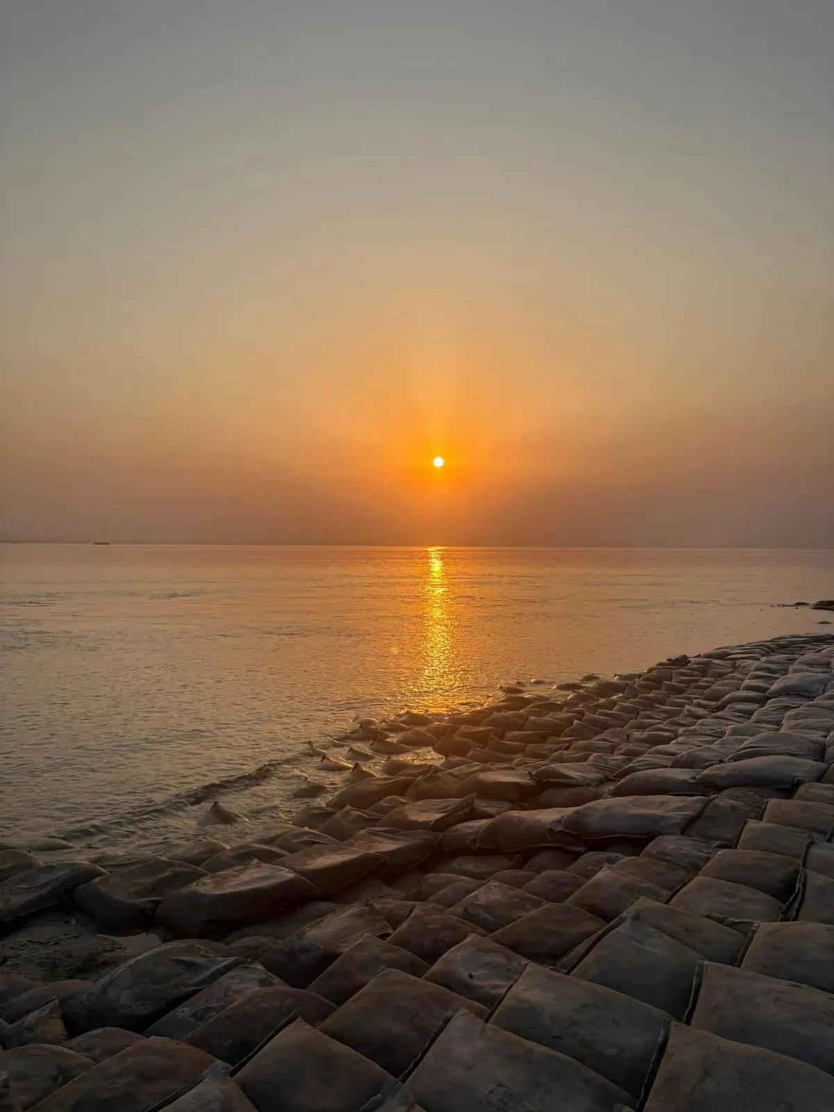 Sun setting over the Meghna River with a geobag revetment in the foreground along the shoreline