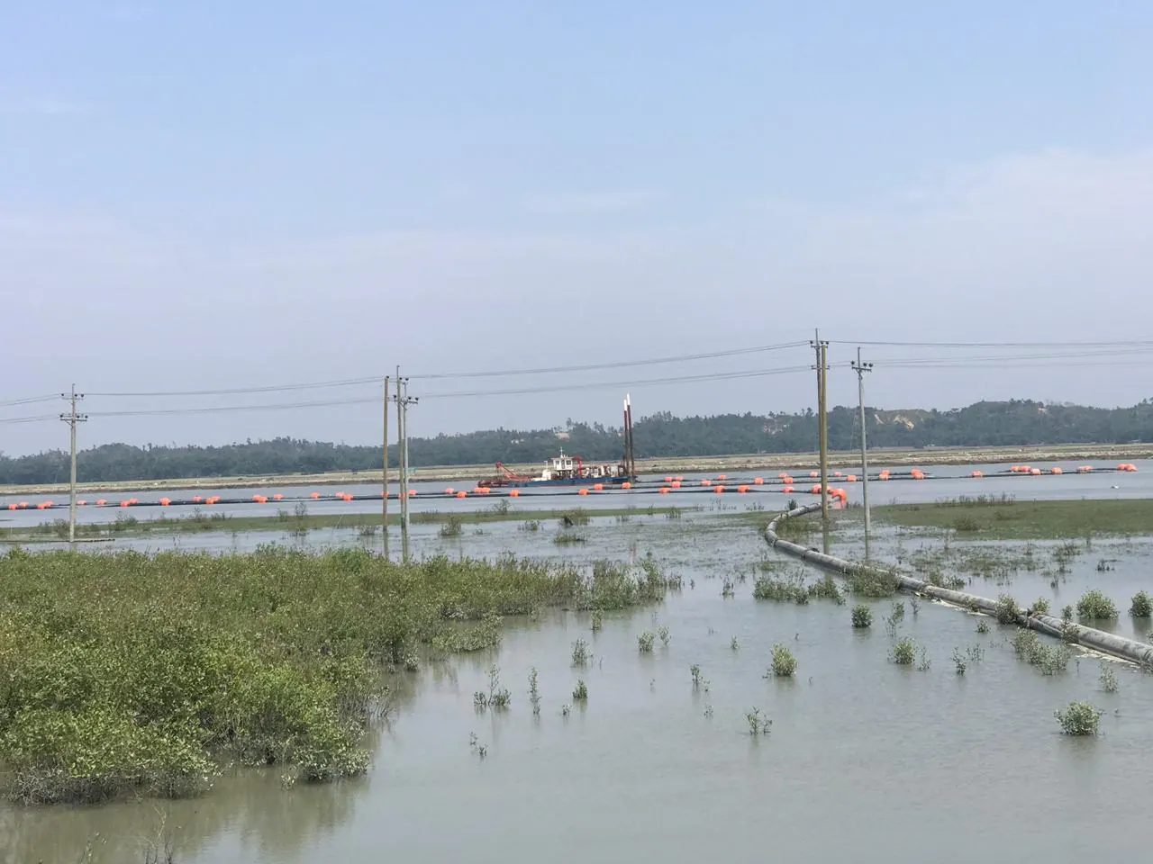 Cutter suction dredger on the Kohelia River with a floating pipeline on orange buoys, seen past flooded scrub
