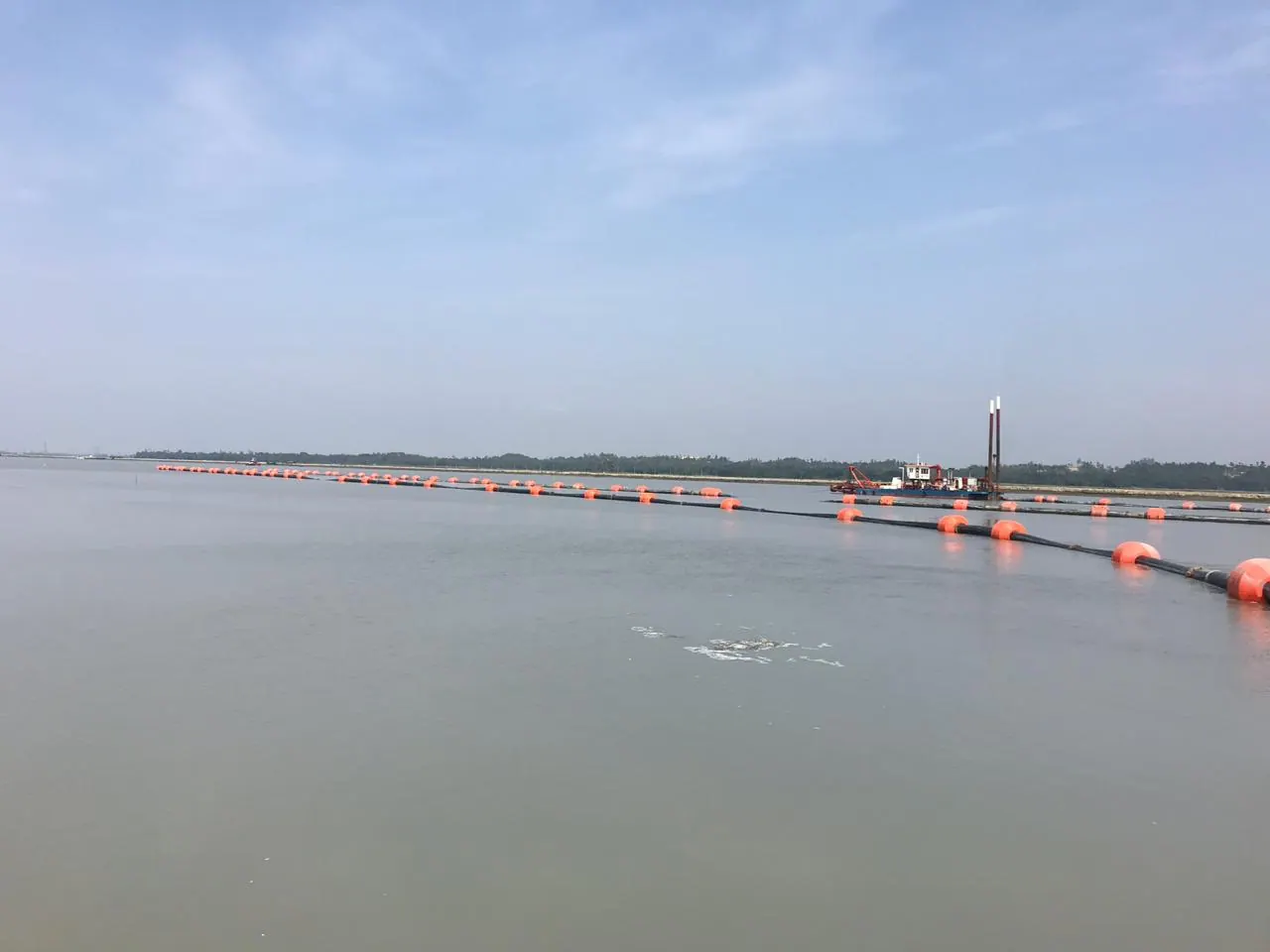 Floating dredge pipeline on orange buoys stretching across calm river water to a cutter suction dredger