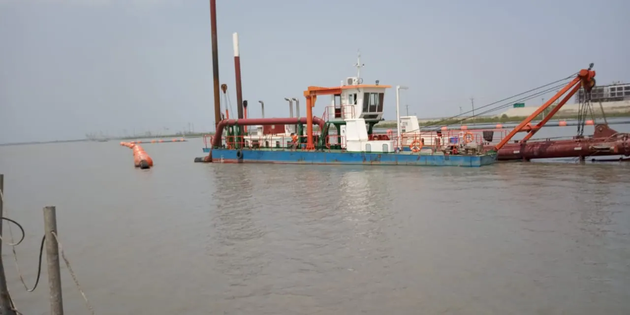 Cutter suction dredger with blue hull, wheelhouse and orange cutter ladder moored on the river, buoyed pipe alongside