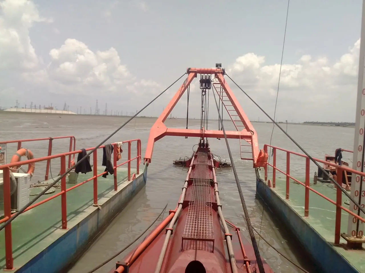 View along the cutter ladder and orange A-frame gantry from the dredger deck, twin pontoon hulls either side