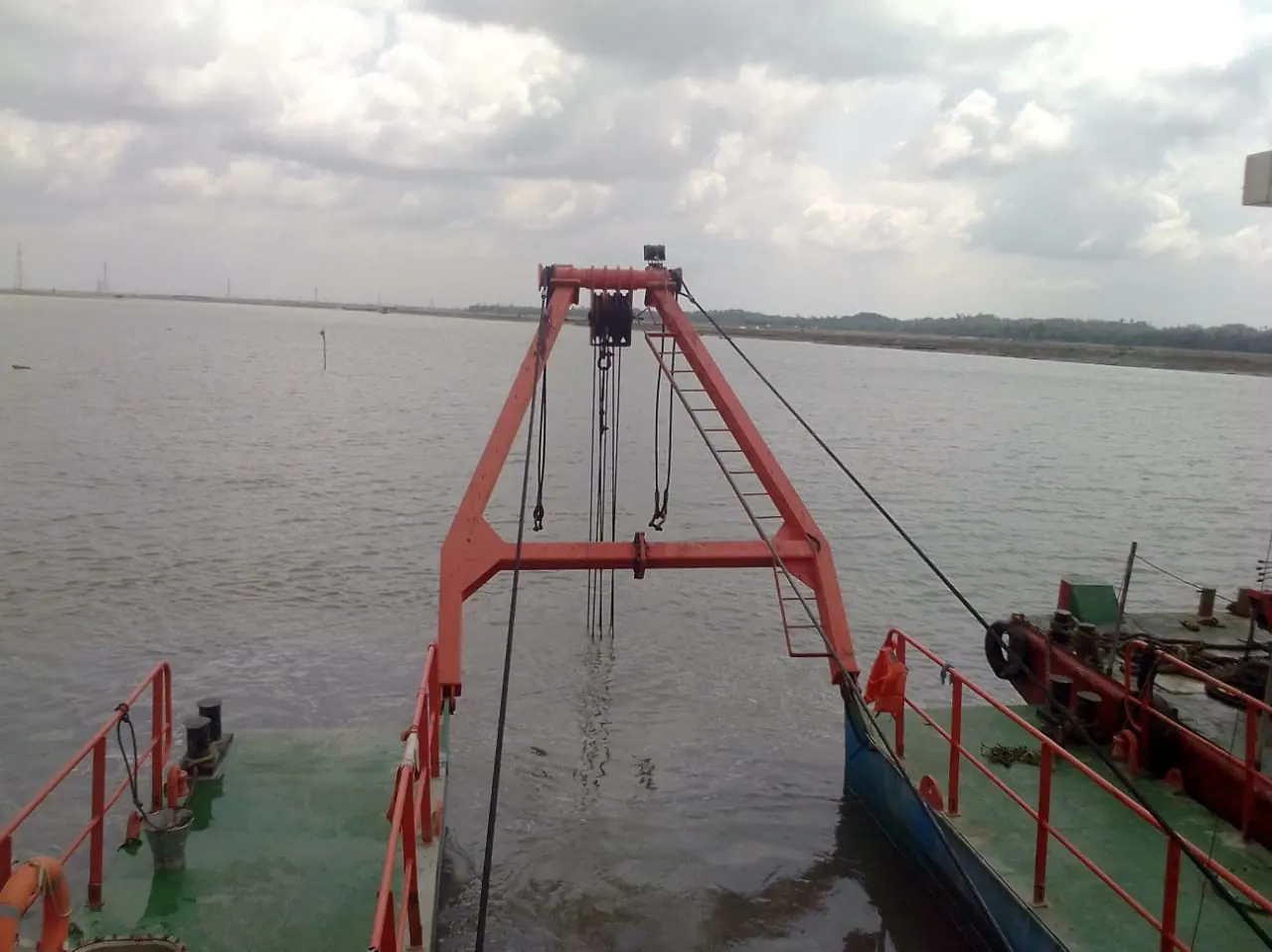 Orange A-frame gantry and hoist cables of a cutter suction dredger raised over grey river water