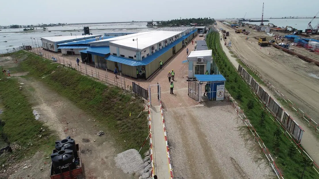 Aerial view of a fenced accommodation camp with blue-roofed prefab buildings, guard house and gate at Matarbari site