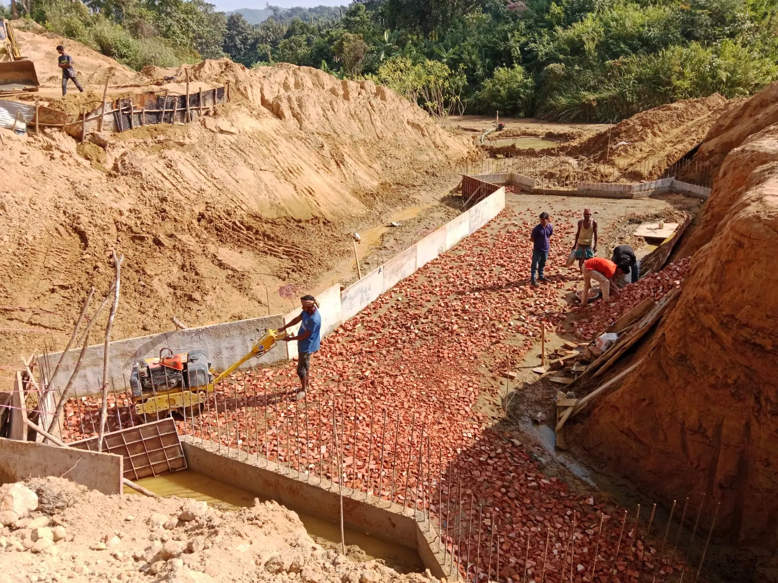 Elevated view of workers spreading brick aggregate and a walk-behind roller compacting it between culvert walls